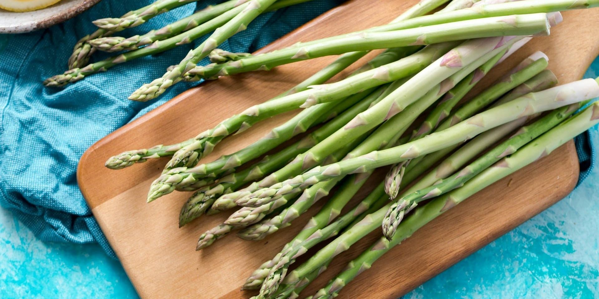Groene asperges op een houten snijplank, klaar om verwerkt te worden in een kookroutine.