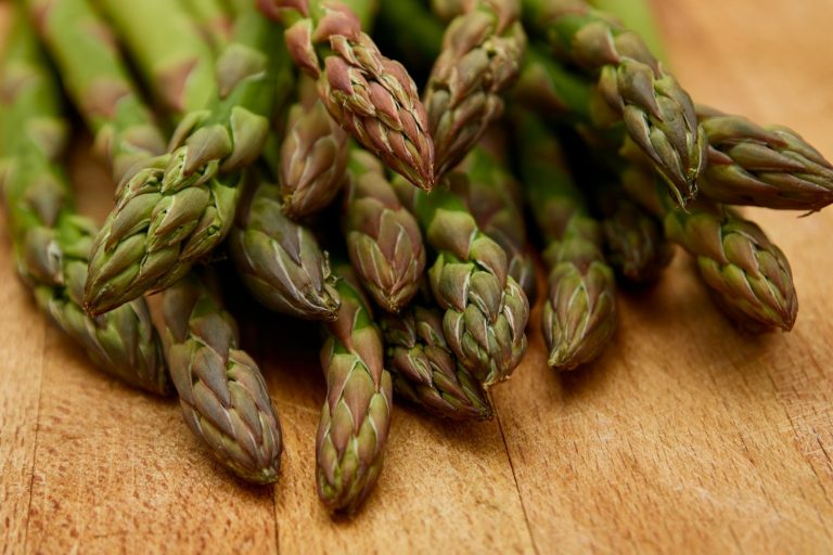 Groene asperges met paarse toppen liggen in een tros op een houten snijplank – gegrilde bijgerechten versterken hun smaak.
