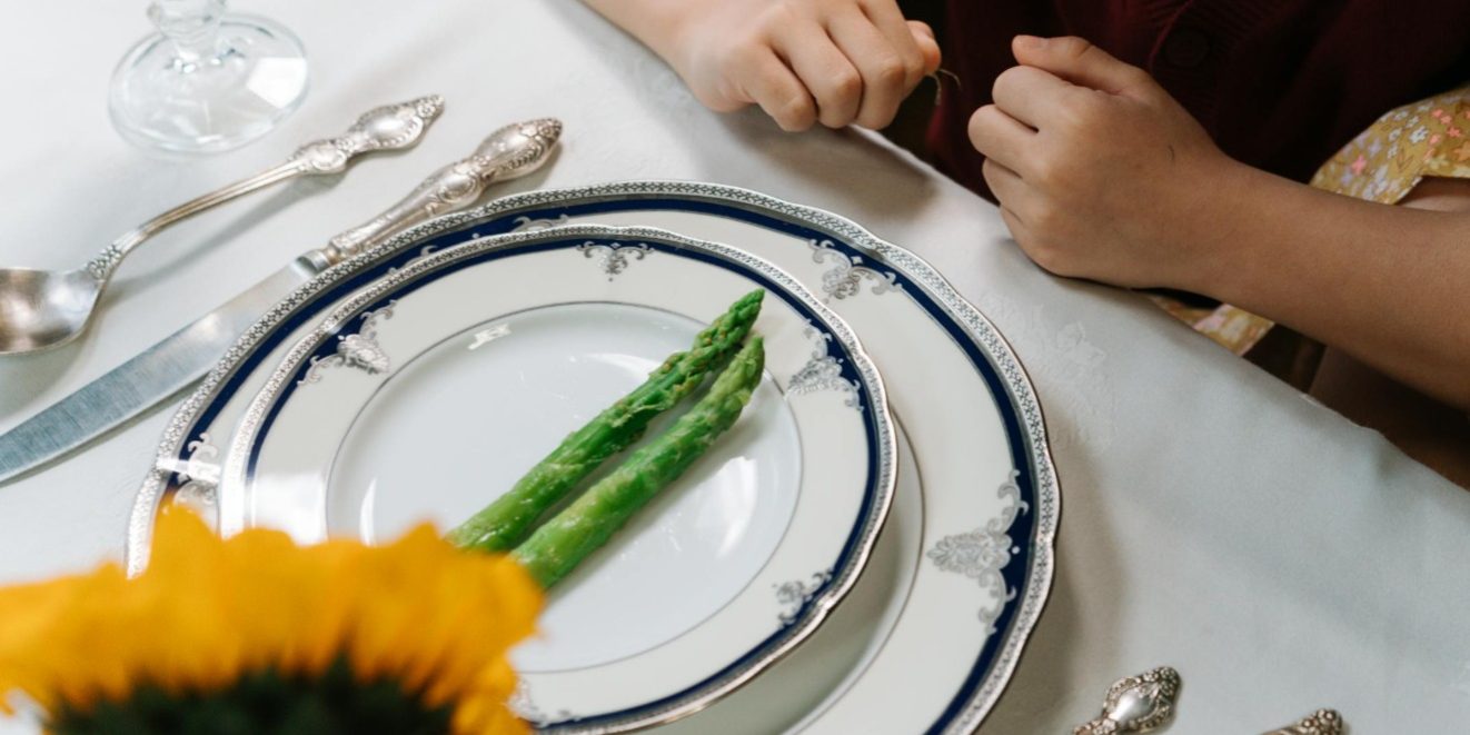 Gekookte groene asperges op een gedekte tafel met klassiek servies en kinderhanden