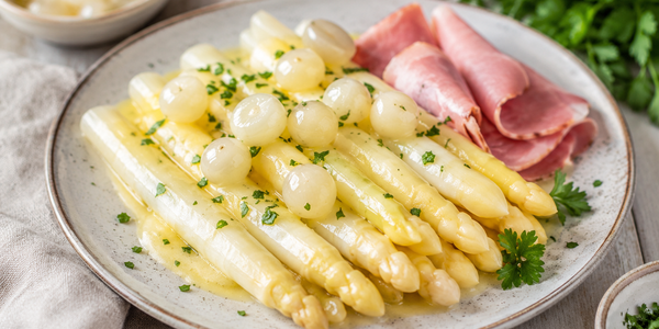 Witte asperges met zilveruitjes, ham en botersaus op een bord geserveerd als klassieke lentemaaltijd Witte asperges met zilveruitjes, ham en botersaus op een bord geserveerd als klassieke lentemaaltijd